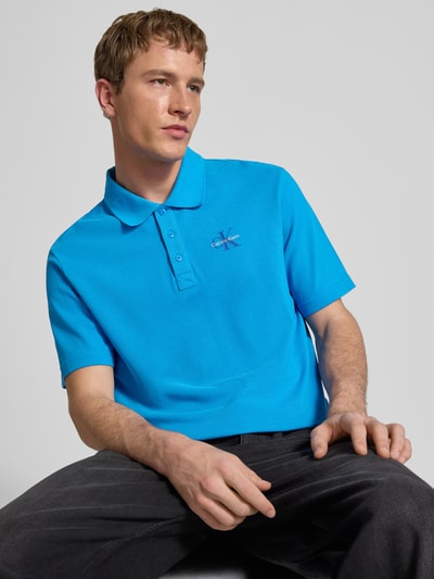Männermodel trägt Easy Fit Poloshirt mit Polokragen von Calvin Klein Jeans, reine Baumwolle, Label-Stitching, leuchtendes Blau, Nahaufnahme Oberkörper.