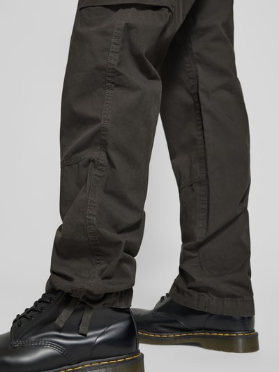 Männermodel trägt Straight Fit Cargohose mit Gesäßtaschen von G-Star Raw aus reiner Baumwolle, in dunklem Braun, Detailaufnahme Beine.