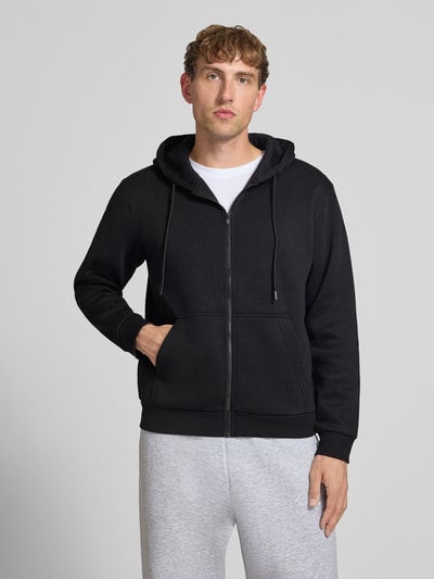 Männermodel trägt Regular Fit Sweatjacke aus Baumwoll-Mix Modell 'BRADLEY' von JACK & JONES in Schwarz mit Kapuze und Känguru-Tasche, Ganzkörperansicht von vorne. Herren Sweatjacke aus Baumwoll-Mix, elastische Abschlüsse, Rückenlänge 67 cm, Ärmellänge 68 cm.