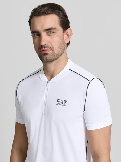 Männermodel trägt Regular Fit T-Shirt mit Stehkragen von EA7 Emporio Armani in Weiß mit Label-Print, Nahaufnahme Oberkörper.