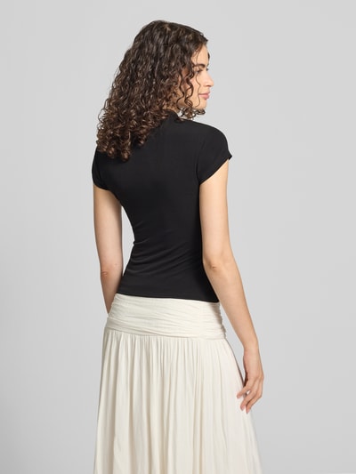 Frauenmodel trägt Slim Fit T-Shirt mit Cut Out von Gina Tricot, schwarzer Material-Mix mit Stretch-Anteil, Stehkragen, Rückenlänge 48 cm bei Größe S, Ganzkörperansicht Rückansicht.