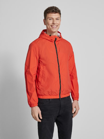 Männermodel trägt Peuterey Jacke mit capuchon Modell 'NIGLE', regular fit, steekzakken, tweewegritssluiting, oranjerood, Ganzkörperansicht von vorne. Ruglengte maat M: 69 cm, schouderbreedte: 47 cm, borstwijdte: 56 cm, mouwlengte: 68 cm.