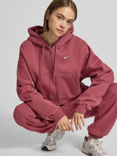 Frauenmodel trägt Regular Fit Sweatjacke aus Baumwoll-Mix von Nike Damen Sweatjacke w kolorze ciemnoróżowym, zamek, kieszeń kangurka, miękka faktura, Nahaufnahme Oberkörper