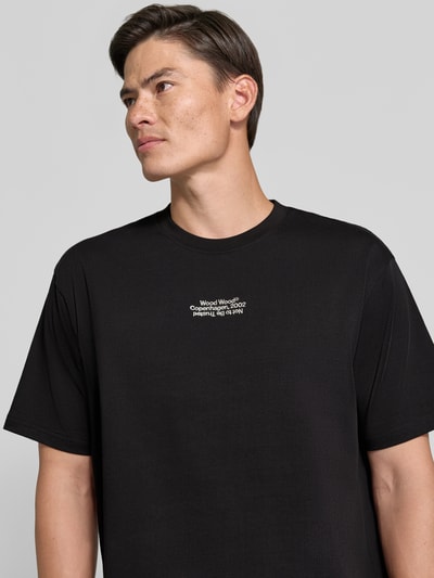 Männermodel trägt Regular Fit T-Shirt aus reiner Baumwolle Modell 'Oliver' von Wood Wood in Schwarz mit Logo-Stitching, Nahaufnahme Oberkörper.