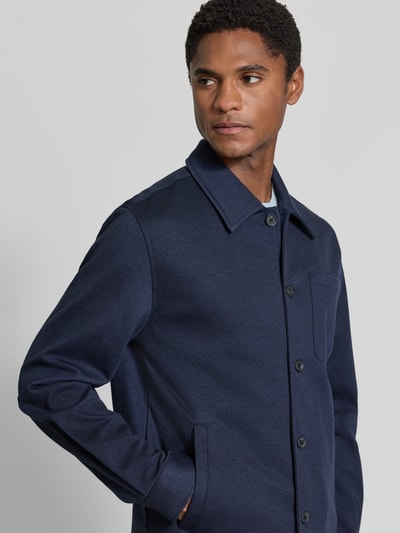 Männermodel trägt Slim Fit Hemdjacke mit Viskose-Anteil von Lindbergh in Dunkelblau mit Umlegekragen, Nahaufnahme Oberkörper. Elastischer Material-Mix, aufgesetzte Brusttasche und Eingriffstaschen, Rückenlänge bei Größe M 70 cm.