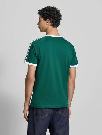 Męski model nosi T-Shirt mit Label-Stitching od adidas Originals w kolorze zielonym, bawełniany miks, krój regular fit, żebrowane wykończenia, okrągły dekolt, długość pleców w rozmiarze M: 74 cm, widok całej sylwetki z tyłu.