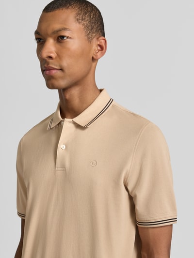 Męski model nosi Slim Fit Poloshirt mit Label-Stitching od bugatti, beżowa bawełna, krój slim fit, detal logo, polo kołnierz, guziki, model 'Käntchen', długość tyłu w rozmiarze M: 67 cm, zbliżenie na górną część ciała.