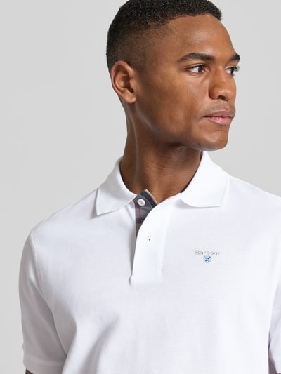 Męski model nosi Regular Fit Poloshirt aus reiner Baumwolle od Barbour, biały, kołnierzyk polo, krótki rękaw, piqué, zbliżenie na górę ciała.