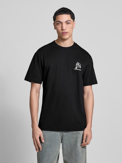 Männermodel trägt Relaxed Fit T-Shirt aus reiner Bio-Baumwolle Modell 'FRED' von Only & Sons, schwarz, Frontprint, Ganzkörperansicht von vorne.