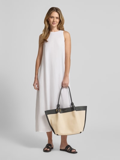 Frauenmodel trägt weißen, ärmellosen Maxikleid und hält Shopper mit Label-Detail Modell 'FINN CANVAS' von Coccinelle, Ganzkörperansicht von vorne.