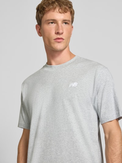 Männermodel trägt ein graues T-Shirt mit Label-Stitching Modell 'ESSENTIALS' von New Balance aus reiner Baumwolle, Nahaufnahme Oberkörper.