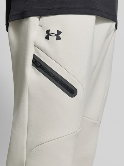 Männermodel trägt Regular Fit Sweatpants mit Logo-Print Modell 'Unstoppable' von Under Armour aus elastischem Material-Mix mit Baumwoll-Anteil, Beintasche mit Reißverschluss, elastischer Bund und Beinabschlüsse, Nahaufnahme Oberschenkel.