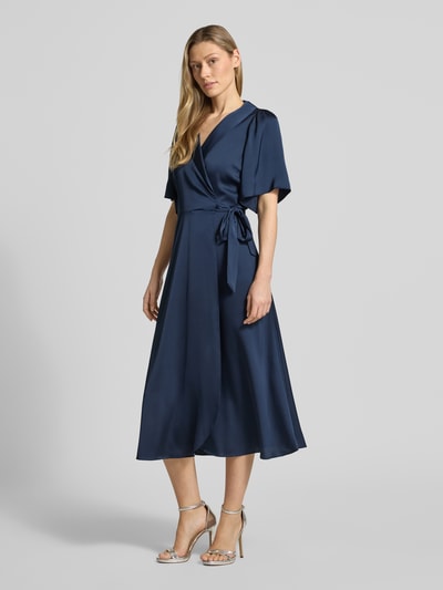 Frauenmodel trägt Midikleid in Wickel-Optik Modell 'VIENNA RAVENNA' von Vila aus dunkelblauem Satin, taillierter Schnitt, V-Ausschnitt, Ganzkörperansicht von vorne. Kontext: Damen Midikleid, Rückenlänge bei Größe 36: 125 cm, Brustweite: 50 cm, Ärmellänge: 30 cm.