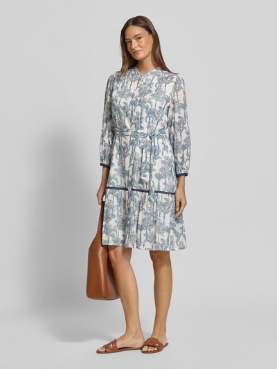 Frauenmodel trägt knielanges Kleid mit Stehkragen Modell 'Milo' von 0039 Italy, floraler Print in Blau, Weiß, Braun, taillierte Passform, Ganzkörperansicht von vorne.