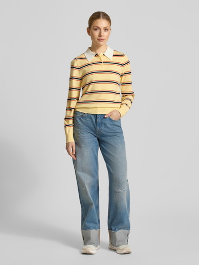 Frauenmodel trägt Regular Fit Poloshirt mit Knopfleiste Modell 'PREGO' von SUNCOO PARIS im Material-Mix mit Lanawoll-Anteil, gelb-weiß gestreift, passt zu Jeans, Damen Poloshirt, Ganzkörperansicht von vorne.