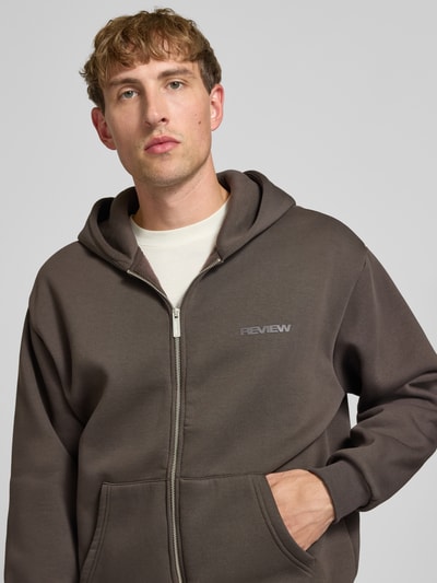 Männermodel trägt Relaxed Fit Sweatjacke aus Baumwoll-Mix mit Label-Detail von REVIEW in Braun, sichtbare Känguru-Tasche, Nahaufnahme Oberkörper