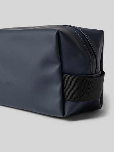 Produktfoto, Wash Bag mit Logo-Detail von Rains in Dunkelblau mit schwarzem Trageriemen, glatte Oberfläche, sichtbares Steckfach, Kontext: Herren Wash Bag, Hauptfach mit Reißverschluss, Steckfach innen, Maße 20x14x11 cm, Schulterriemen 14 cm