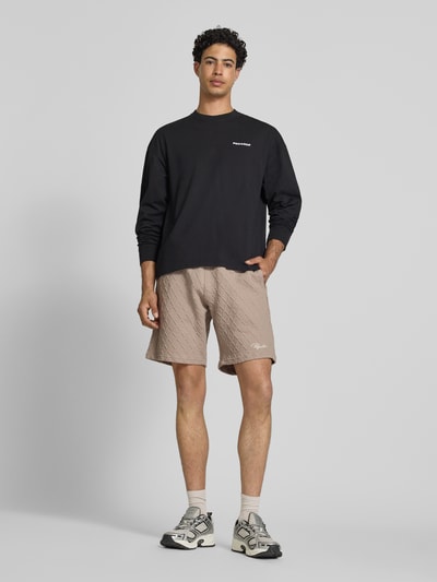 Männermodel trägt beige Relaxed Fit Shorts mit Strukturmuster Modell 'Jovren' von Pegador aus Elastischer-Material-Mix, Ganzkörperansicht von vorne.