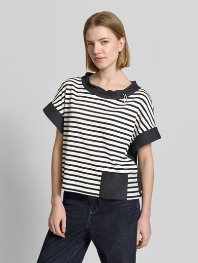 Frauenmodel trägt T-Shirt mit Rundhalsausschnitt und Kordelzug von Marc Cain, Gerader-Schnitt, Label-Detail, Eingrifftasche, Rückenlänge 55 cm bei Größe 36, schwarz-weiß gestreift mit schwarzen Akzenten, Ganzkörperansicht von vorne.