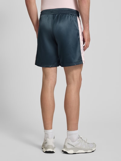 Männermodel trägt Shorts aus Satin mit Label-Stitching und elastischem Bund von BLKVIS, Regular-Fit, dunkelblau-rosa, Ganzkörperansicht Rückansicht.