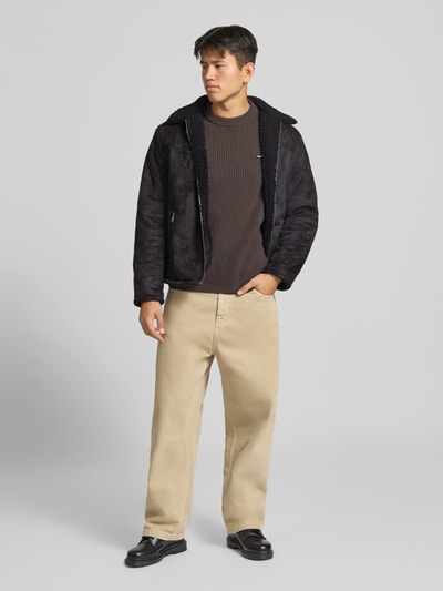 Männermodel trägt Jacke in Leder-Optik mit Reißverschlusstaschen von REVIEW in Schwarz, Regular Fit, Beige Hose, Ganzkörperansicht von vorne.