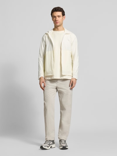 Männermodel trägt Jacke mit Stehkragen und Logo von Salomon in Offwhite, Regular Fit, Reißverschluss, dezentes Markenzeichen, Ganzkörperansicht von vorne. Rückenlänge 70 cm, Schulterbreite 52 cm, Brustweite 61 cm, Ärmellänge 66 cm.