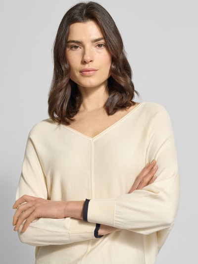 Modelka kobieca nosi Strickpullover aus Viskose-Mix mit V-Ausschnitt od comma, kremowy, krój regular fit, rękawy z kontrastowym paskiem, zbliżenie na górną część ciała.