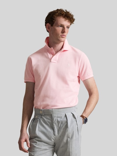 Männermodel trägt Regular Fit Poloshirt aus reiner Baumwolle van Polo Ralph Lauren in effen lichtroze, piqué structuur, logo-detail, polokraag, korte knoopsluiting, korte mouwen met geribde boorden, zijsplitten, asymmetrisch, voorkant volledige lichaamsopname.
