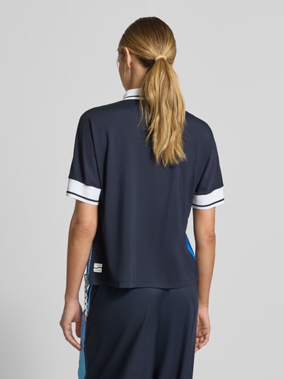 Frauenmodel trägt Regular Fit Bluse aus reinem Lyocell mit Polokragen von Marc Cain, dunkelblau mit weißen Details, Ganzkörperansicht Rückansicht. Damen Bluse mit Allover-Motiv-Print, kurzärmelig, Tunnelzug im Bund, Länge bei Größe 36: 60 cm, Ärmellänge: 39 cm.