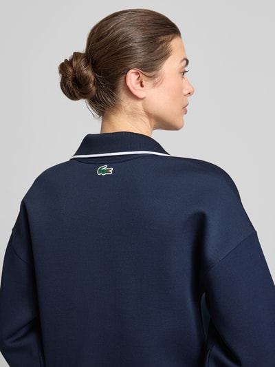 Frauenmodel trägt Regular Fit Sweatshirt mit Kontraststreifen von Lacoste, Optik: Unifarben, Passform: Regular-Fit, Polokragen, V-Ausschnitt, Ärmelform: Langarm, Ärmelabschluss: Gerippt, Rumpfabschluss: Gerippt, glatte dunkelblaue Textur, Ganzkörperansicht Rückansicht.