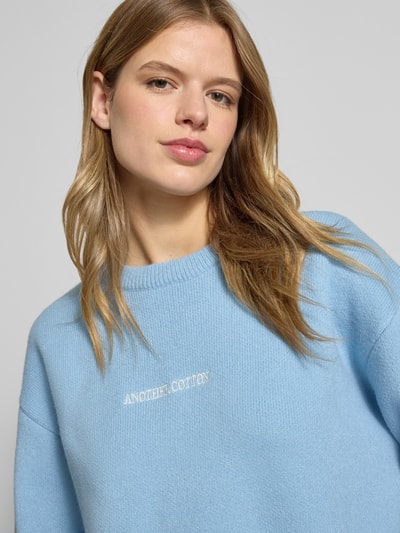 Frauenmodel trägt Oversized Strickpullover mit Rückenmotiv von ANOTHER COTTON LAB in Hellblau, Rundhalsausschnitt, Label-Stitching, Nahaufnahme Oberkörper. Rückenlänge bei Größe S: 62 cm, Ärmellänge bei Größe S: 57 cm.
