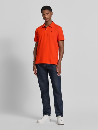 Männermodel trägt Regular Fit Poloshirt aus reiner Baumwolle von Tom Tailor in kräftigem Orange, blaue Jeans, weiße Schuhe, Ganzkörperansicht von vorne. Herren Poloshirt von Tom Tailor.