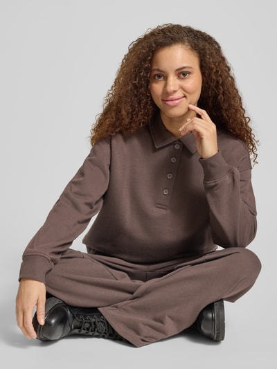 Vrouwenmodel draagt Sweatshirt mit Polokragen und Knopfleiste van Gina Tricot, dames sweatshirt regular fit, polokraag, knoopsluiting, verlaagde schouders, vooraanzicht zittend, detailopname bovenlichaam.