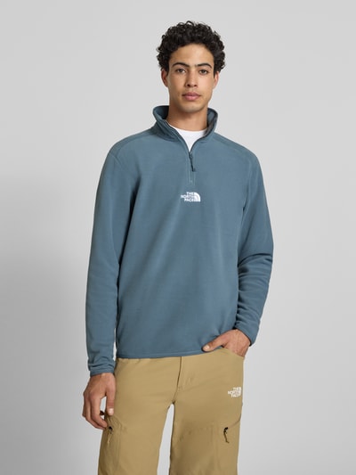 Męski model nosi Fleecepullover mit Reißverschluss Modell 'GLACIER' von The North Face, krój regular fit, stójka, niebieskoszary, gładka faktura, logo z przodu, długość tyłu w rozmiarze M: 70 cm, długość rękawa w rozmiarze M: 67 cm, widok całej sylwetki z przodu.