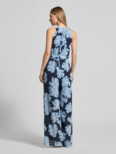 Modelka nosi Jumpsuit mit Bindegürtel und Plisseefalten od Christian Berg Cocktail, ciemnoniebieski z jasnoniebieskim wzorem kwiatowym na lekkim szyfonie, krój slim fit, okrągły dekolt, wiązany pasek w talii, tylny dekolt w kształcie łezki, długość tyłu w rozmiarze 36: 36 cm, szerokość w rozmiarze 36: 34 cm, całkowita długość w rozmiarze 36: 157 cm, długość nogawki wewnętrznej: 83 cm, widok całej sylwetki od tyłu.