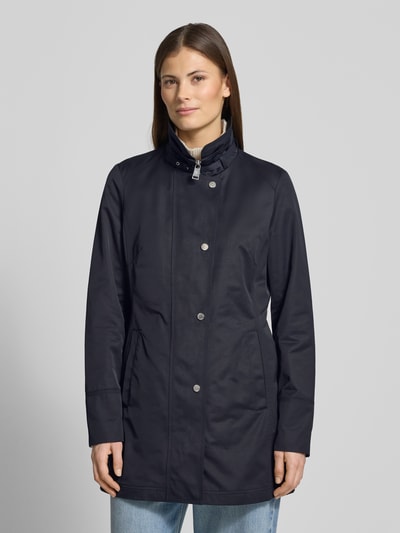 Frauenmodel trägt Trenchcoat mit Stehkragen und Eingrifftaschen von Fuchs Schmitt in Dunkelblau, taillierter Baumwoll-Mix, Ganzkörperansicht von vorne.