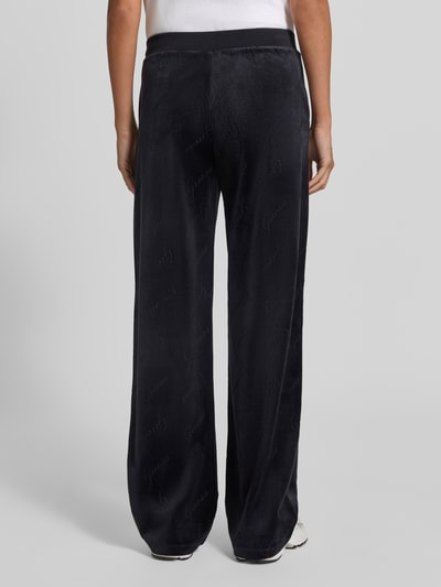 Frauenmodel trägt Straight Fit Sweatpants mit elastischem Bund Modell 'LOREN' von GUESS, dunkle Farbe, samtige Textur, Ganzkörperansicht Rückansicht, Damen Sweatpants, Material-Mix mit Stretch-Anteil.