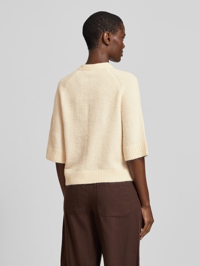 Frauenmodel trägt Cardigan mit Eingrifftasche Modell 'Dathena' von OPUS, cremefarben, gerader Schnitt, materielle Struktur erkennbar, Ganzkörperansicht Rückansicht. Material-Mix mit Mohair-Anteil, rundhals, Knopfleiste, gerippte Abschlüsse, Rückenlänge 51 cm, Ärmellänge 36 cm.