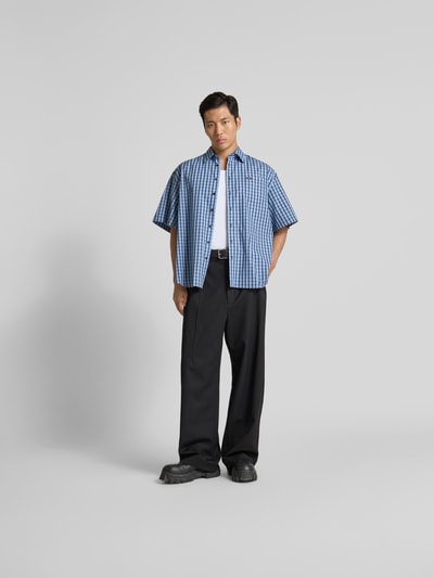 Männermodel trägt Oversized Freizeithemd mit Brusttasche von VETEMENTS in Blau-Kariert, Baumwolle, Kurzarm, Ganzkörperansicht von vorne.