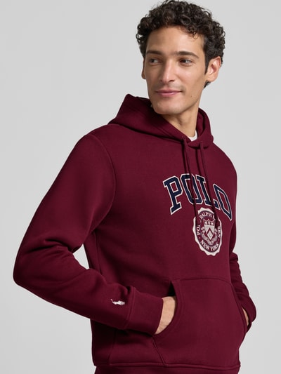 Männermodel trägt Relaxed Fit Hoodie aus Baumwoll-Mix von Polo Ralph Lauren in Dunkelrot mit Logo-Print, weiche Textur, Nahaufnahme Oberkörper. Herren Sweatshirt von Polo Ralph Lauren.