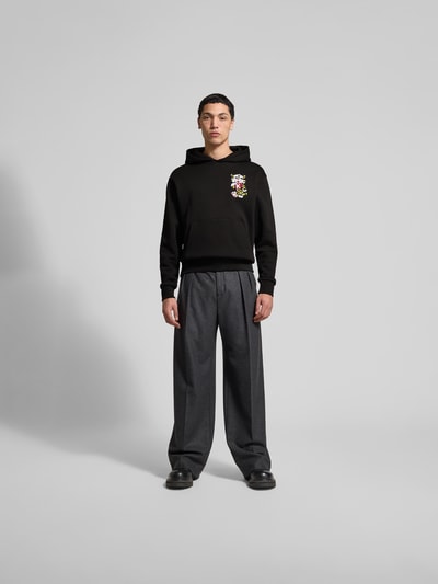 Männermodel trägt Oversized Hoodie aus reiner Baumwolle von Kenzo, lockere Passform, Label-Stitching, Känguru-Tasche, elastische Abschlüsse, Herren Sweatshirt, dunkle Töne, glatte Textur, Ganzkörperansicht von vorne.