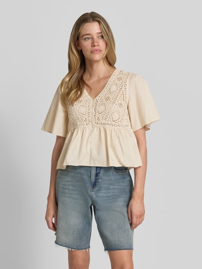 Frauenmodel trägt Blusentop mit Häkelspitze Modell 'SALVI' von Bash aus Reine Baumwolle in Regular-Fit mit V-Ausschnitt, kurzen Ärmeln, Knopfleiste, beigefarbene Textur, Rückenlänge 50 cm, Nahaufnahme Oberkörper.