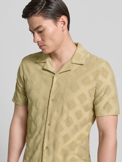 Männermodel trägt Slim Fit Poloshirt mit Strukturmuster von Fynch-Hatton aus Baumwoll-Mix in Beige mit Reverskragen, Nahaufnahme Oberkörper.