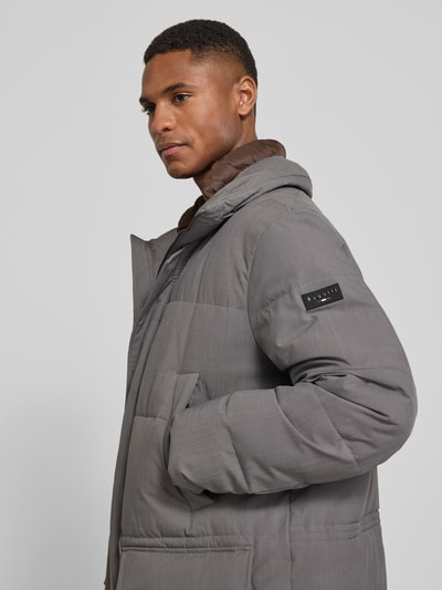 Męski model nosi parka mit kapuze von bugatti w kolorze szarym, z kapturem, stójką, wpuszczanymi i kieszeniami z patką, krój regular fit, szerokość ramion w rozmiarze 52: 48 cm, szerokość klatki piersiowej w rozmiarze 52: 61 cm, długość rękawów w rozmiarze 52: 70 cm, długość tyłu: 90 cm, zamek błyskawiczny kryty, zdjęcie w półzbliżeniu od przodu