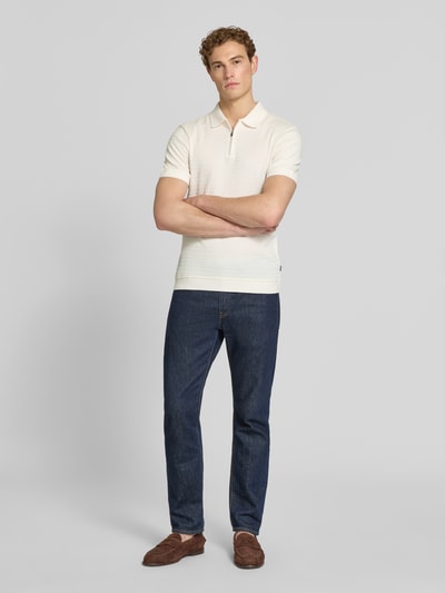 Männermodel trägt Slim Fit Poloshirt mit Reißverschluss Modell 'Franciscojose' von JOOP! Collection aus reiner Baumwolle in Creme, Ganzkörperansicht von vorne.