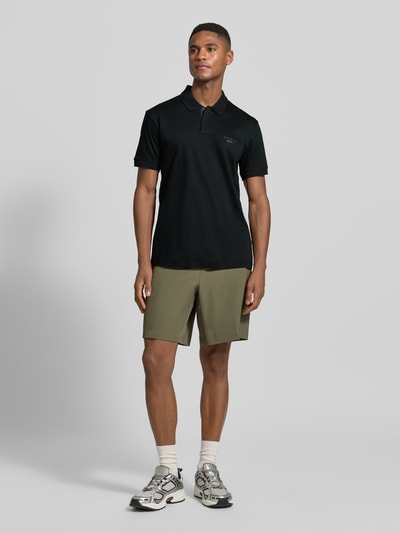 Männermodel trägt Regular Fit Poloshirt aus reiner Baumwolle Modell 'PS Spirit 70 Plk' von BOSS Green X PORSCHE in Schwarz, Ganzkörperansicht von vorne.