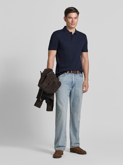 Męski model nosi Regular Fit Poloshirt aus Baumwoll-Mix Modell 'PARLAY 240' od BOSS, gładki granatowy kolor, krótki rękaw, label patch, kołnierzyk polo, dekolt w serek, dwuguzikowe zapięcie, krój regular fit, zdjęcie całej sylwetki od przodu.