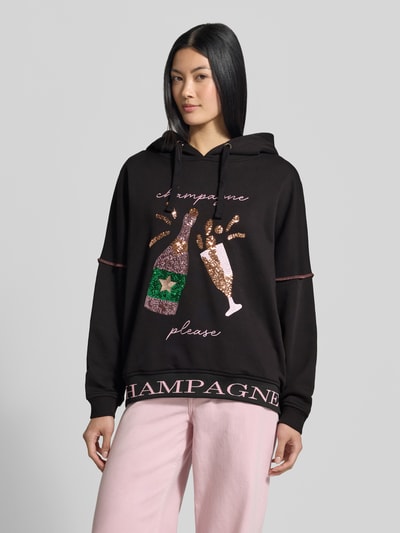 Frauenmodel trägt Hoodie aus reiner Baumwolle von miss goodlife in Schwarz mit Pailletten-Besatz, lockere Passform, elastische Abschlüsse, Ganzkörperansicht von vorne.