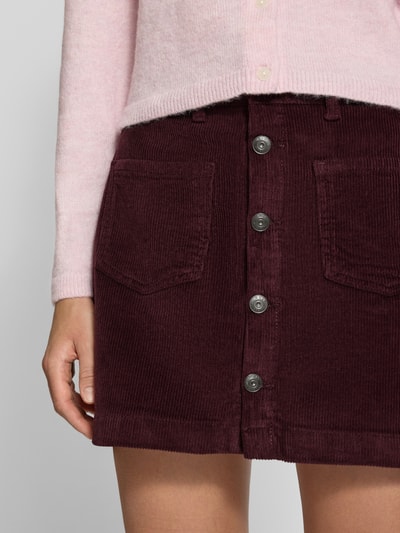Kobiece model prezentuje spódnicę mini z mieszanki bawełny model 'AMAZING' od ONLY w kolorze bordowym, widok z przodu, zbliżenie na górną część spódnicy. Spódnica mini damska marki ONLY.