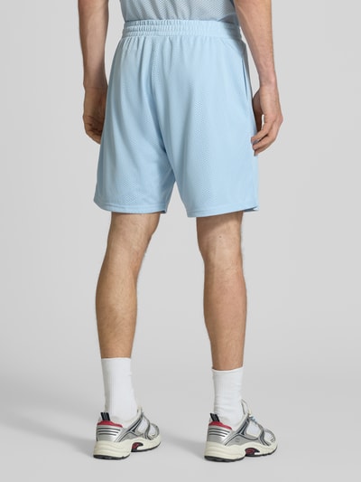 Männermodel trägt Shorts aus Mesh mit Logo-Print von REVIEW in Hellblau, Loose-Fit, Elastikbund, Seitliche Eingrifftaschen, Ganzkörperansicht Rückansicht.